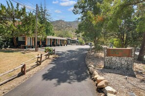 A motel with a stone sign, paved driveway, and surrounding trees. - Moro RM3 Sequoia Motel- AC, Pool, WiFi, 10min SNP (Three Rivers)