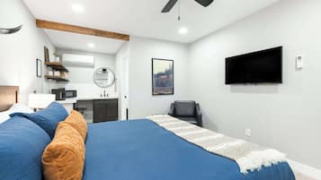 Un dormitorio con cama, ventilador de techo, televisor montado, escritorio con silla y espejo.