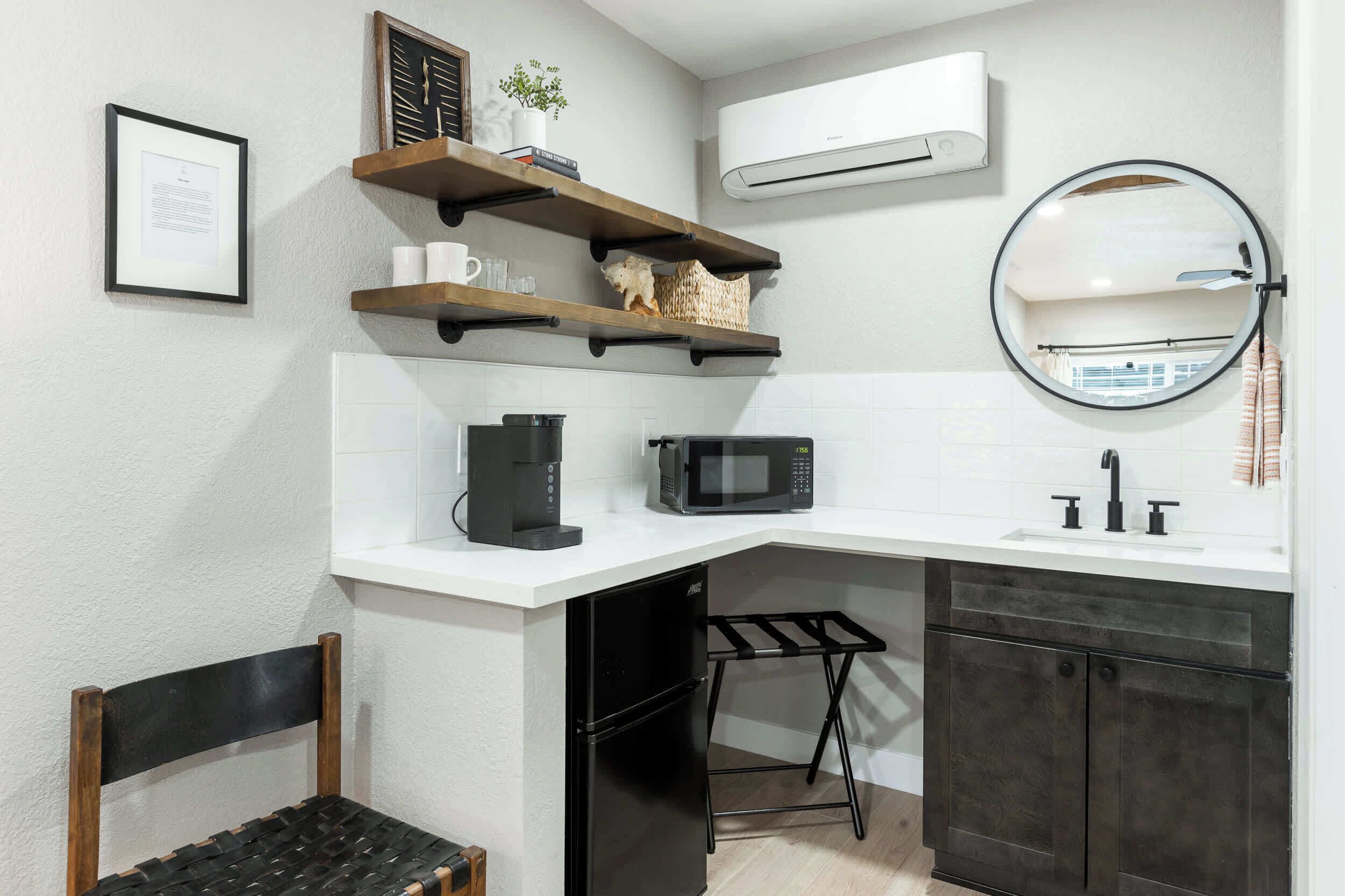 A compact kitchen with a white countertop, a black refrigerator, a microwave, a coffee maker, and a small stool.