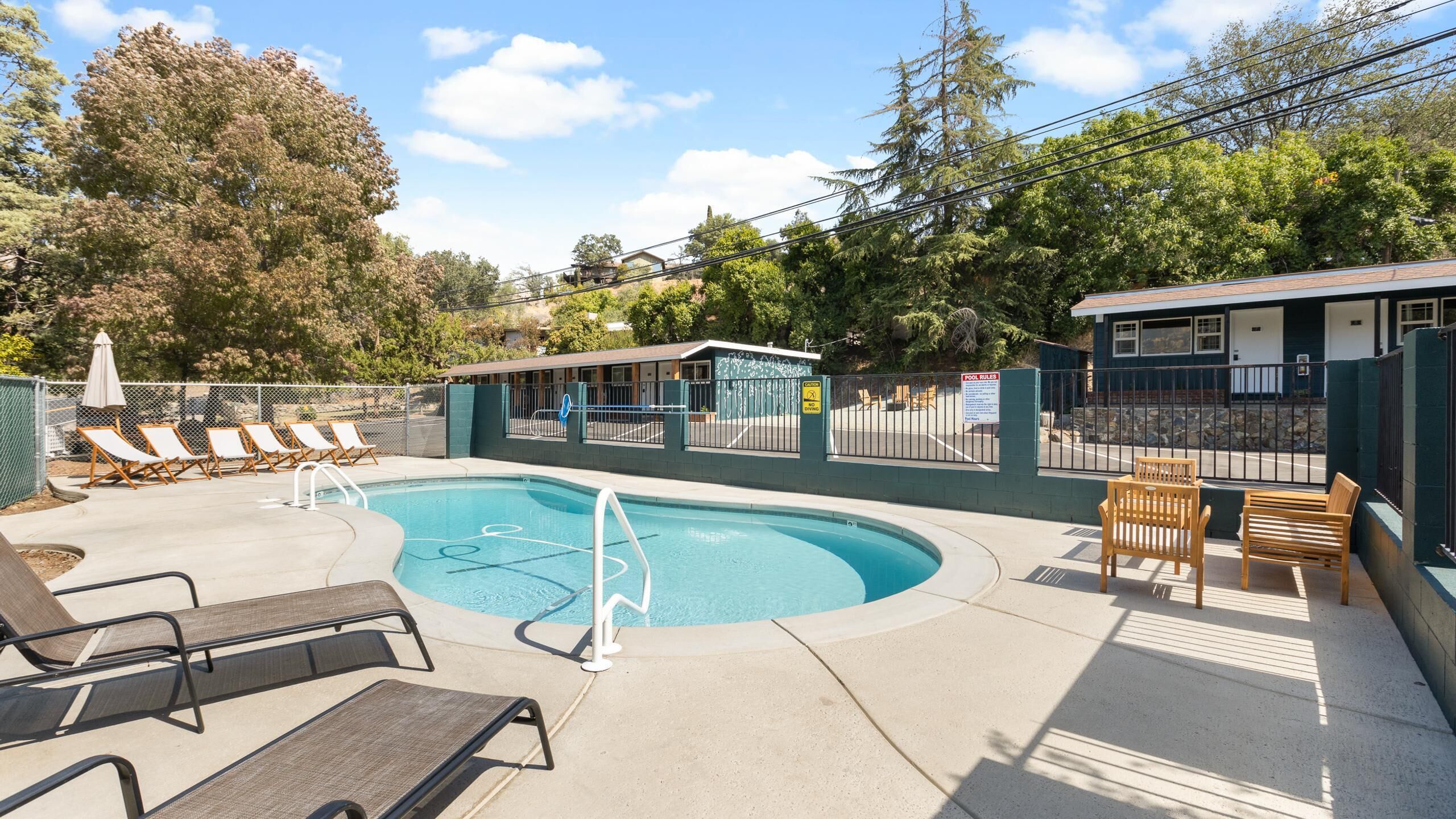 A swimming pool with lounge chairs, a fenced area, and a small building with a sign.