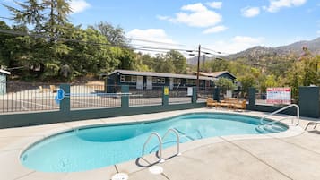 Una piscina con un puesto de socorrista, una zona de estar cubierta y montañas al fondo.