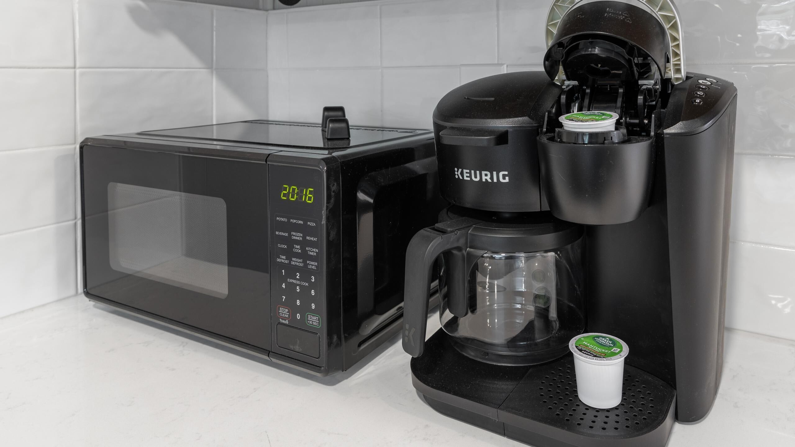 A Keurig coffee maker with a pod, a microwave, and a coffee pot on a countertop.