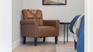 A brown leather armchair with a patterned throw blanket, a framed painting on the wall, and a blue blanket on a bed. - Sequoia Motel King RM6, AC, Pool, WiFi 10 Min SNP (Three Rivers)