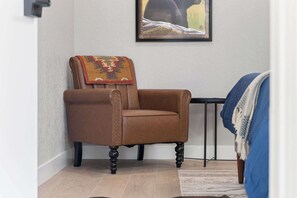 A brown leather armchair with a patterned throw blanket, a framed painting on the wall, and a blue blanket on a bed. - Sequoia Motel King RM6, AC, Pool, WiFi 10 Min SNP (Three Rivers)