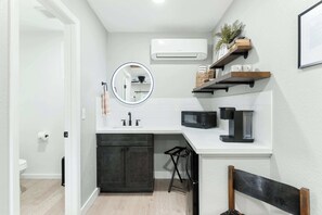 A compact kitchen with a white countertop, a black microwave, and a sink. There are wooden shelves above the counter and a small stool. - Sequoia Motel King RM6, AC, Pool, WiFi 10 Min SNP (Three Rivers)