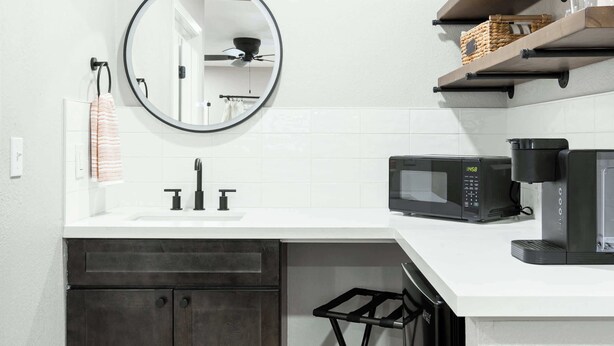 A modern kitchen with a white countertop, a black microwave, a coffee maker, and a hanging towel.
