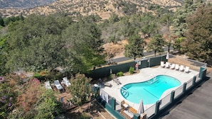 A swimming pool with lounge chairs, surrounded by a fence, with a mountainous backdrop.