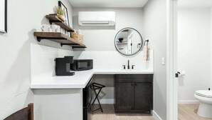 A modern bathroom with a white countertop, a black microwave, a dark cabinet, and a round mirror. - The Rae Sequoia Motel RM5 (Three Rivers)