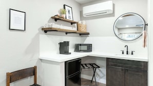 A compact kitchen with a microwave, coffee maker, and a small refrigerator. There are wooden shelves above the counter with various items, and a round mirror above the sink. - The Rae Sequoia Motel RM5 (Three Rivers)