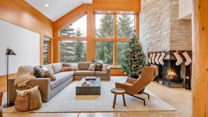 A modern living room with a large sectional sofa, a coffee table, a fireplace with stockings, and a Christmas tree. - Alpine chalet w/ AC, hot tub, media (Whistler)
