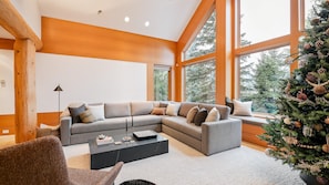 A modern living room with a sectional sofa, a coffee table, and a large window with a view of trees.