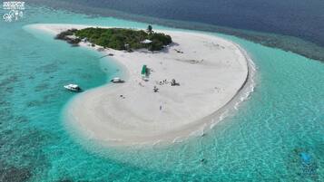 An aerial view of a tropical island with a clear turquoise lagoon, a sandy beach, and a small cluster of buildings surrounded by lush greenery.