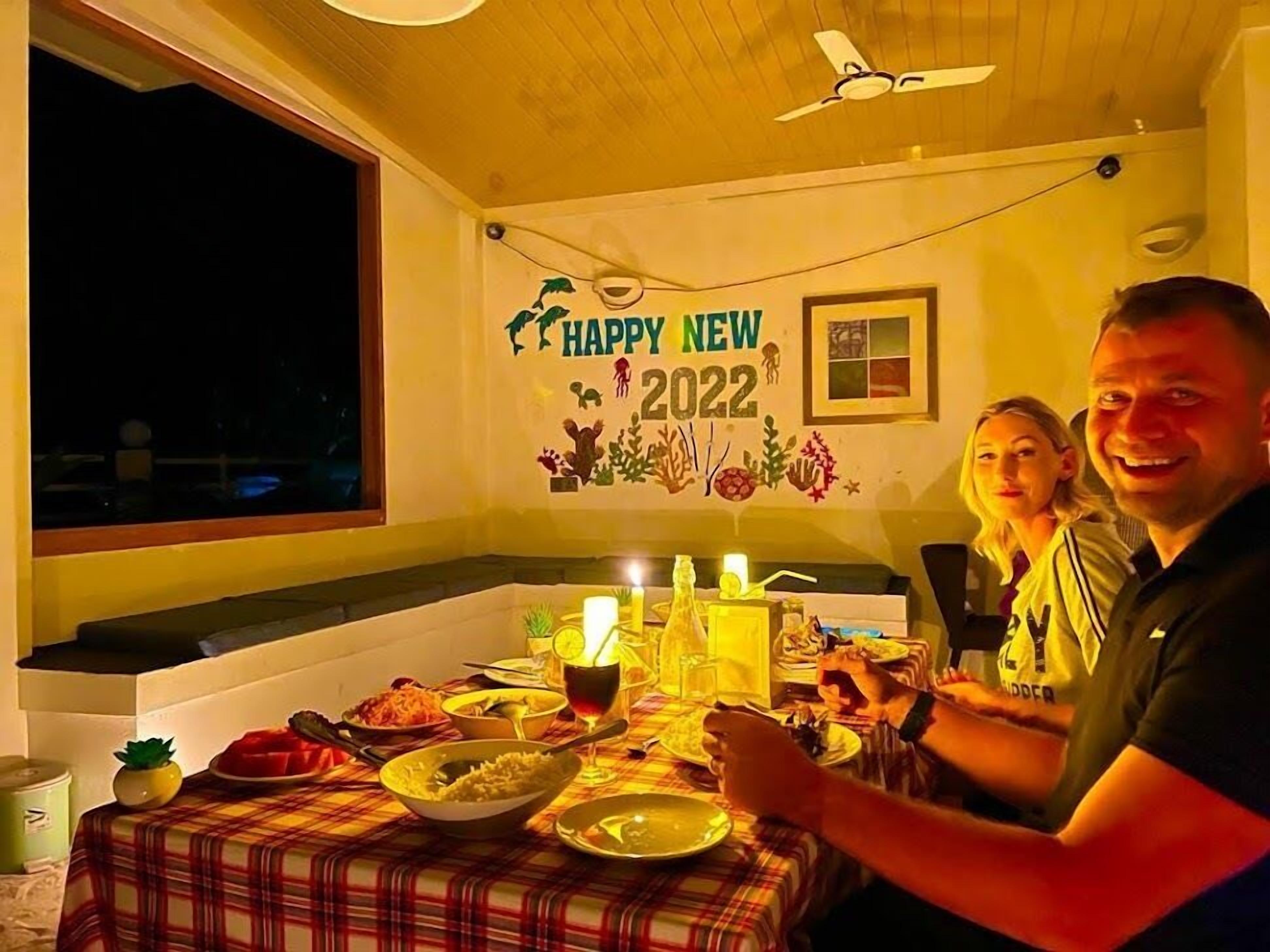 Ein Essbereich mit Tisch für zwei Personen, einer Wanddekoration mit der Aufschrift 'Happy New 2022' und einem Fenster mit Blick auf die dunkle Außenwelt.