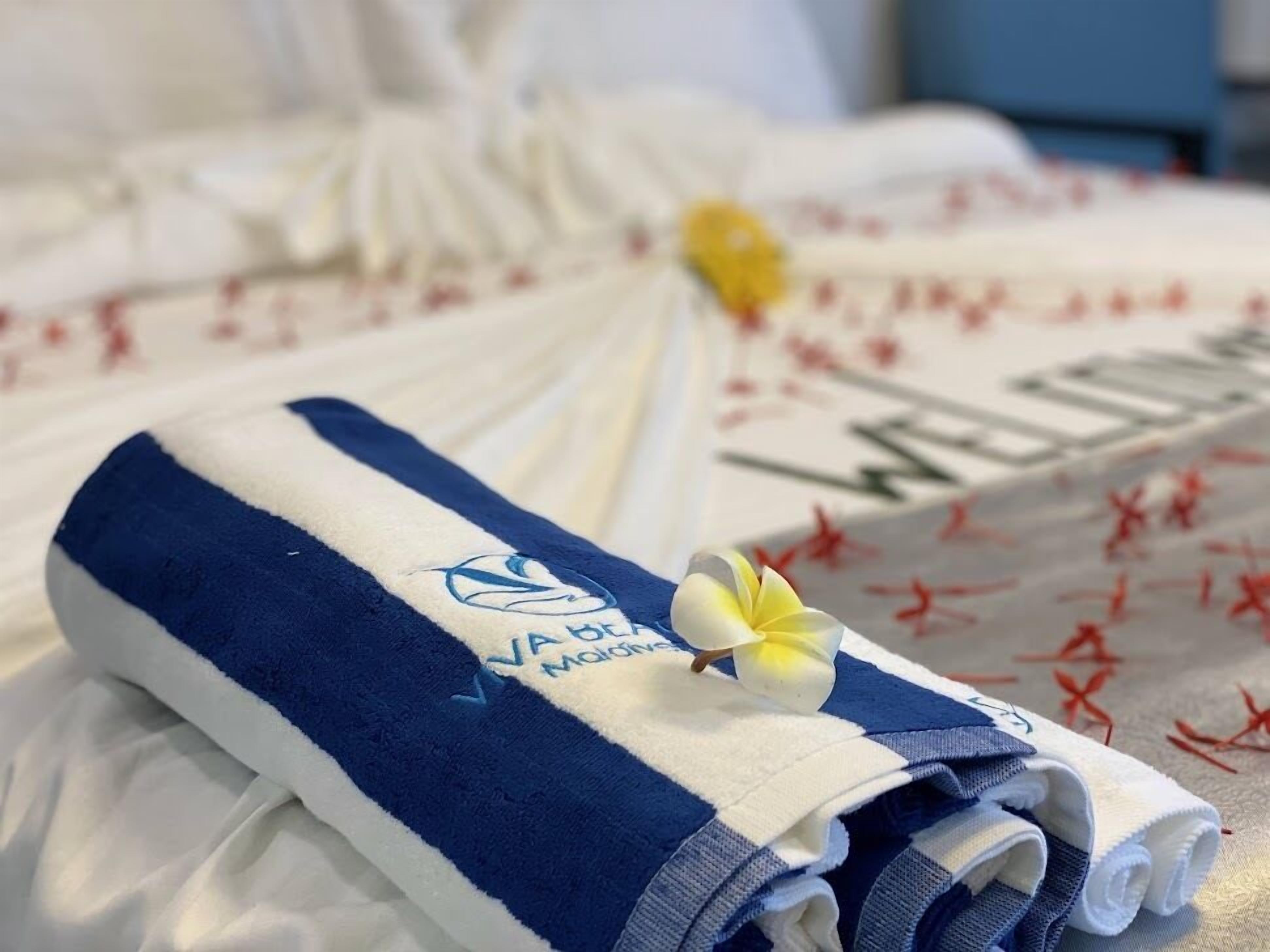 A neatly folded towel with a logo and a flower on a bed with a floral-patterned bedspread.