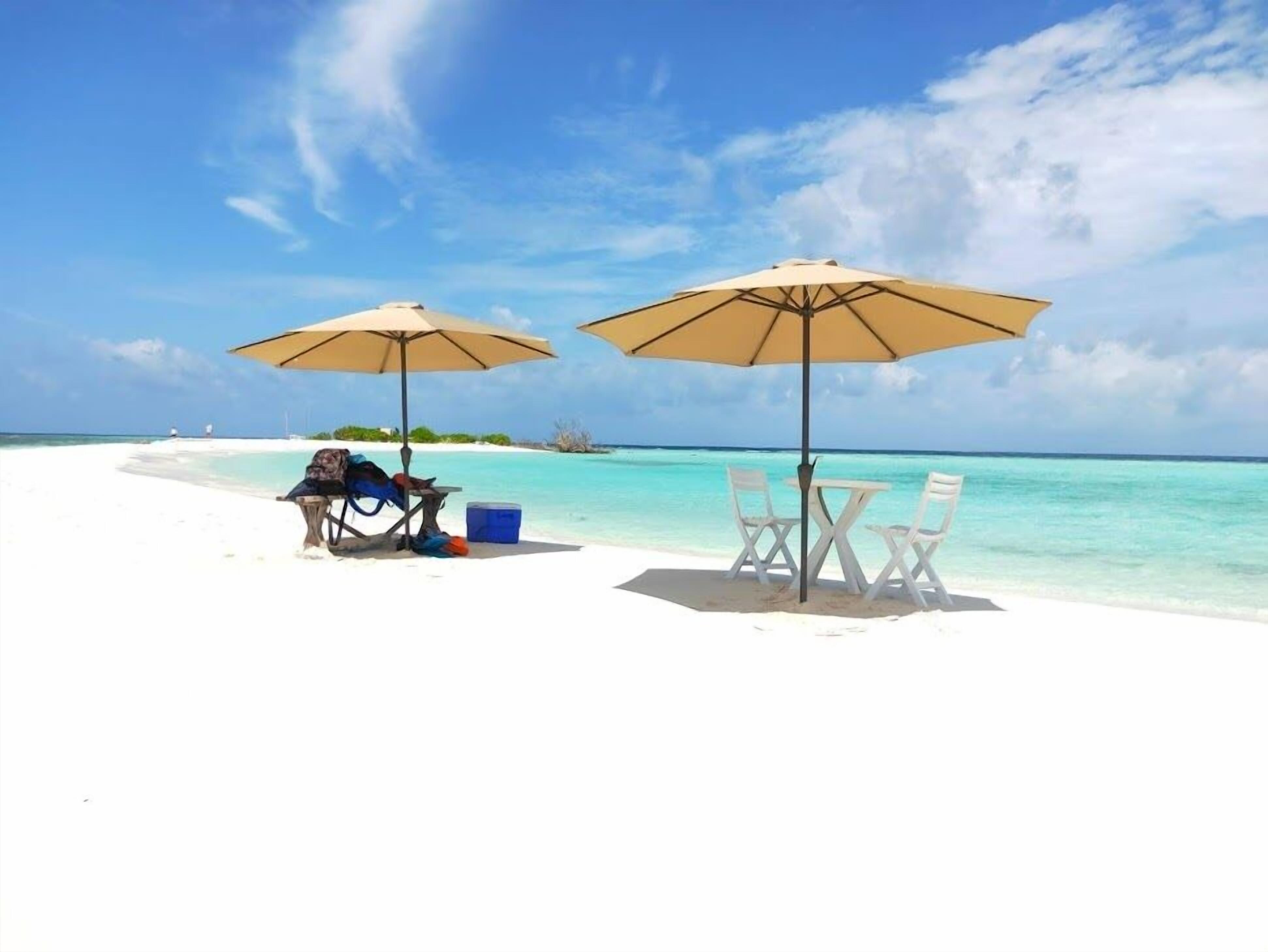 A beach with two umbrellas, a table, and chairs.