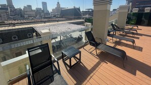 Een terras op het dak met lounge fauteuils en uitzicht op een stadsbeeld.
