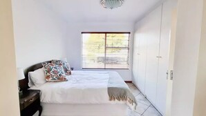 A bedroom with a bed, a nightstand, a wardrobe, and a window with blinds. - Stylish one bed Apartment in Strydom Park - 2168 (Johannesburg)