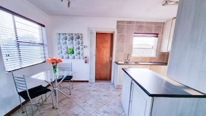 A modern kitchen with a dining area, featuring a table and chairs, a vase with flowers, and a door leading to another room. - Stylish one bed Apartment in Strydom Park - 2168 (Johannesburg)