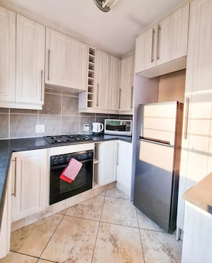A kitchen with white cabinets, a black stove, a microwave, and a stainless steel refrigerator.