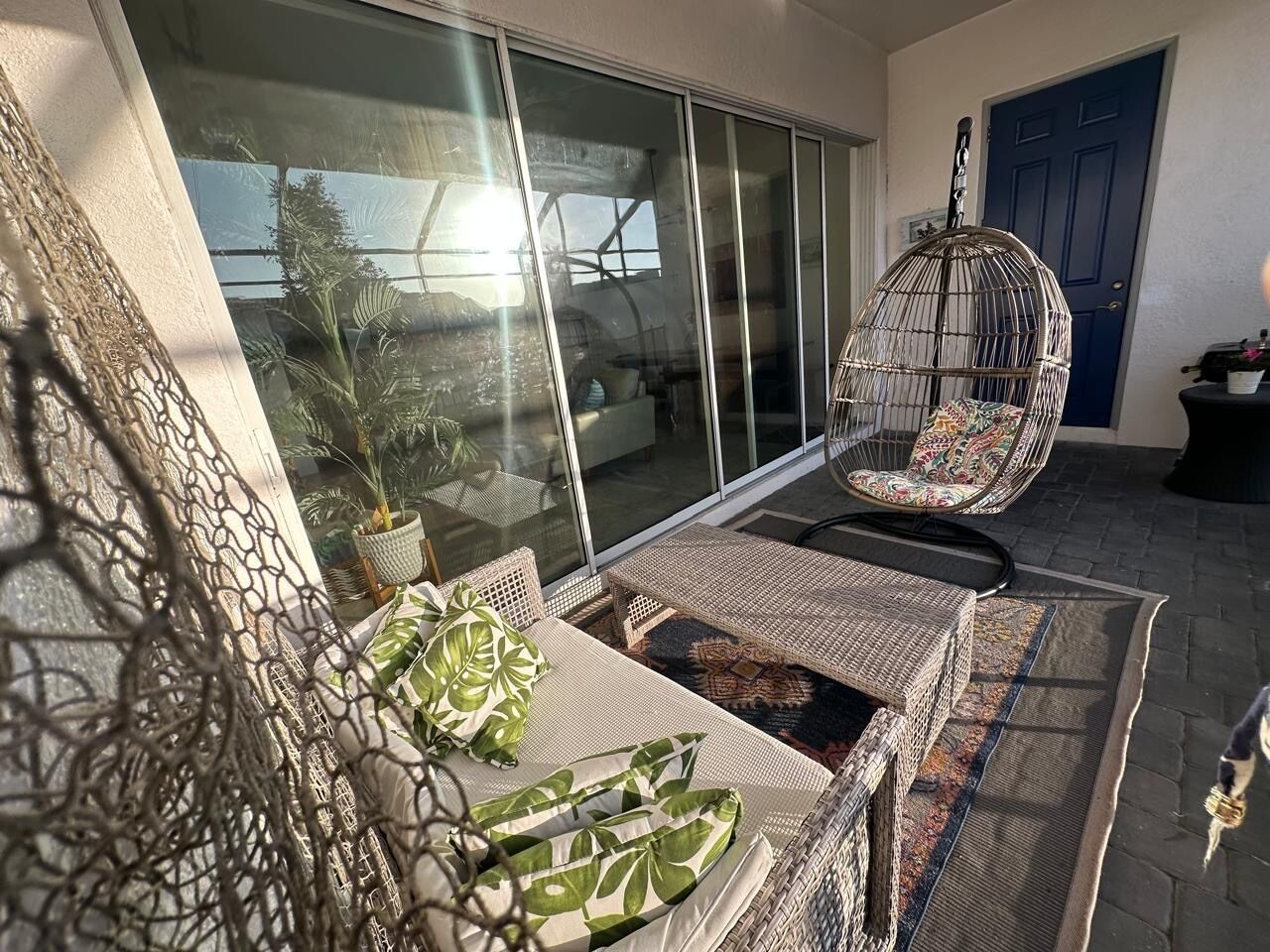 Un balcon agrémenté de meubles en osier, d’un fauteuil suspendu et d’une plante en pot.