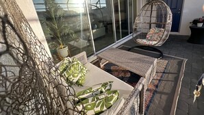 A balcony with wicker furniture, a hanging chair, and a potted plant.
