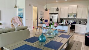 A modern kitchen with white cabinets, a stainless steel refrigerator, and a dining area with a wooden table and blue placemats.