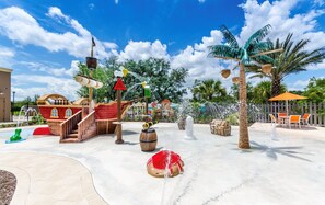 Un espace de jeux aquatiques avec un bateau de pirates, des palmiers et une fontaine.
