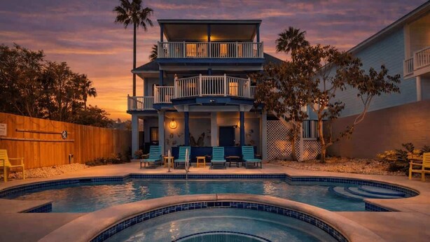 Un edificio de dos pisos con piscina, mobiliario exterior y cerramiento de madera.