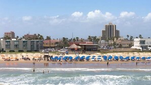 Una playa con sombrillas, un edificio y una estructura alta al fondo.
