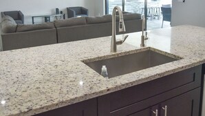 A modern kitchen with granite countertops, dark cabinetry, and a large sink. - New Canal Access Pool Home w/Outdoor Oasis/Kayaks (Cape Coral)