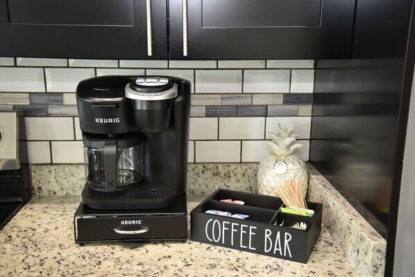 Una cafetera Keurig sobre una encimera de cocina, junto a una barra de café con un letrero.