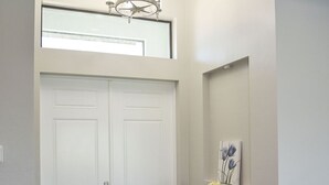 A hallway with a wooden floor, a white door, a console table with a vase and a picture, and a chandelier. - New Canal Access Pool Home w/Outdoor Oasis/Kayaks (Cape Coral)