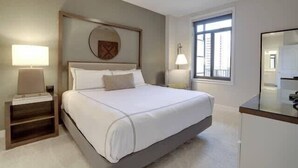 Une chambre moderne avec un grand lit, deux tables de chevet avec des lampes, un ventilateur de plafond et une fenêtre avec des stores.