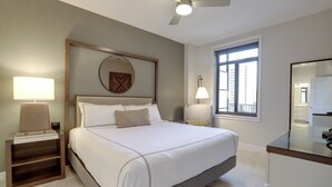 Een moderne hotelkamer met een groot bed, bedlampen, een plafondventilator en uitzicht op de stad door een raam.