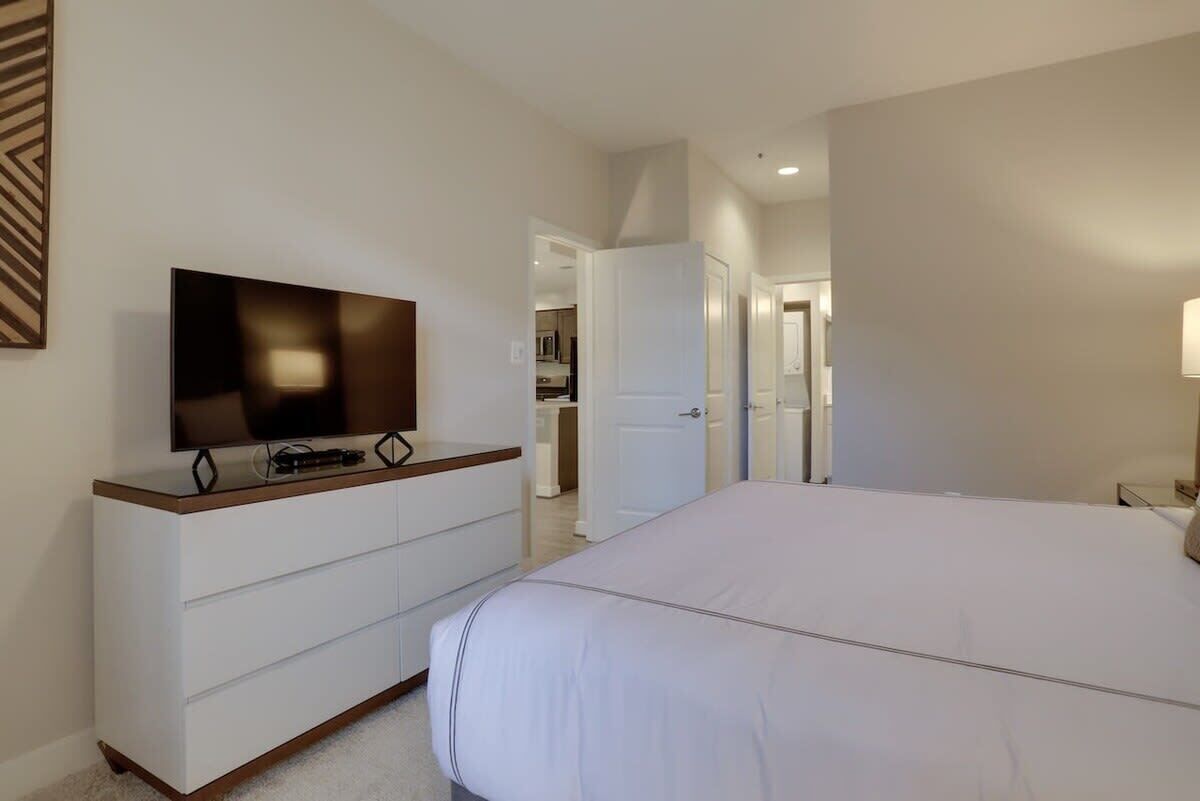A bedroom with a large bed, a TV on a dresser, and a door leading to a bathroom.
