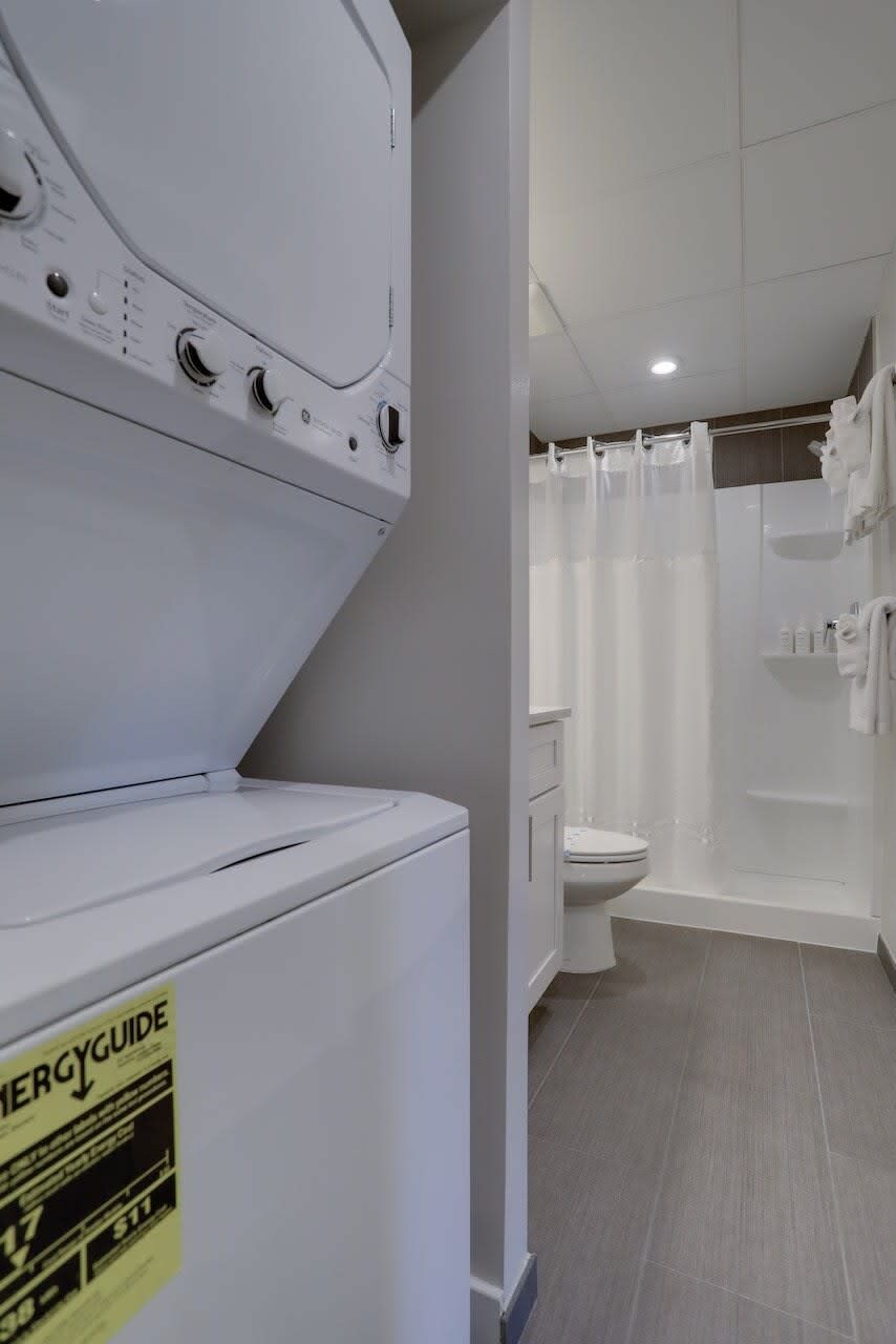 A laundry area with a white washer and dryer, a toilet, and a shower curtain in a bathroom.