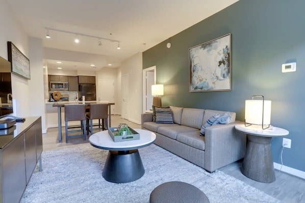 A modern living room with a grey sofa, a round coffee table, and a dining area in the background.