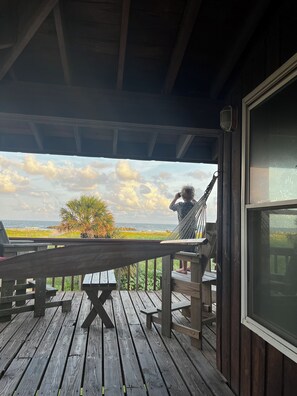 Une terrasse en bois avec un hamac, une table et une vue sur l’océan.