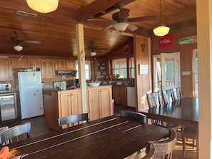 A wooden cabin interior with a kitchen, dining area, and a ceiling fan.