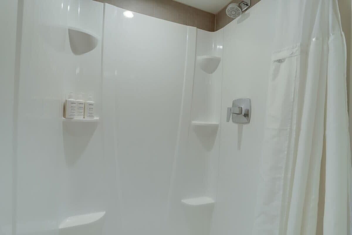 A modern shower area with a white tiled wall, a showerhead, and a control panel.