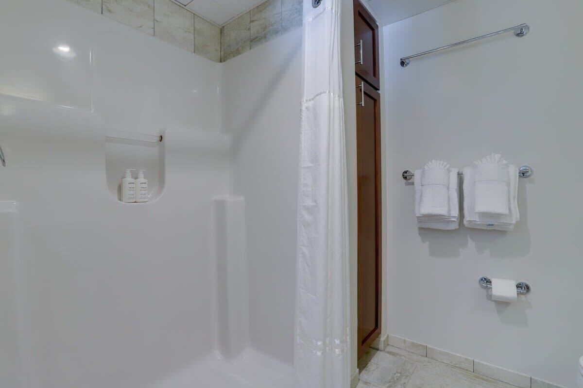 A bathroom with a shower, a towel rack with towels, and a toilet paper holder.
