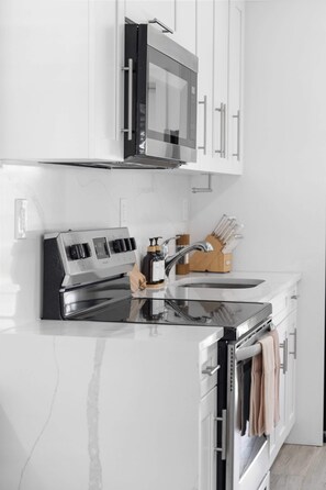 A modern kitchen with stainless steel appliances, white cabinetry, and a wooden utensil holder. - PALM14 | delightful oasis in Pompano Beach (Pompano Beach)