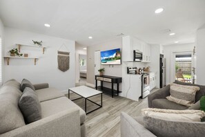 A modern living room with a sofa, a coffee table, and a TV. There is a kitchen area with cabinets and a refrigerator. - PALM14 | delightful oasis in Pompano Beach (Pompano Beach)