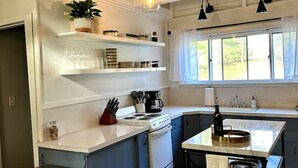 A modern kitchen with white cabinetry, a central island, and pendant lighting. - Esopus Creek Cottage (Saugerties)