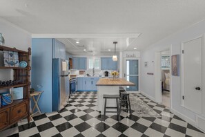 Een moderne keuken met blauwe kastjes, een zwart-wit geruit vloertje en een centraal eiland met krukken.