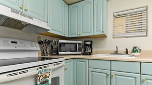A kitchen with teal cabinets, a microwave, a coffee maker, and a bag of premium coffee.