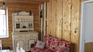 Een gezellig interieur van een chalet met een houten wand, een witte kast met keukengerei en een comfortabele bank met een rood-wit patroon.