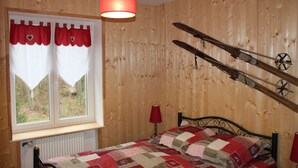 Een slaapkamer met een houten wandpaneel, een bed met quilt, een raam met gordijnen, en een paar ski's bevestigd aan de muur.
