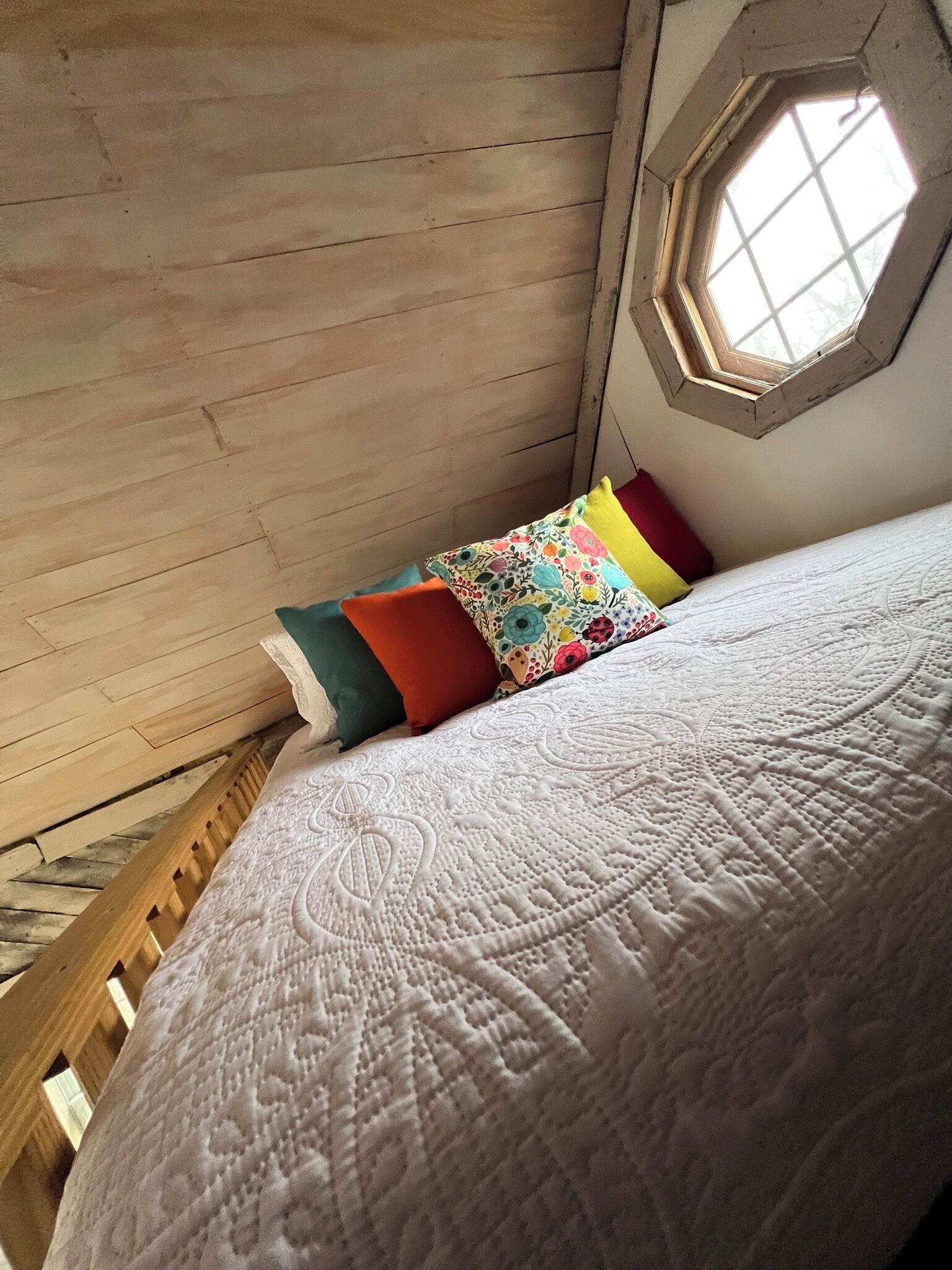 A bedroom with a wooden sloped ceiling, a white quilted bedspread, and colorful pillows.