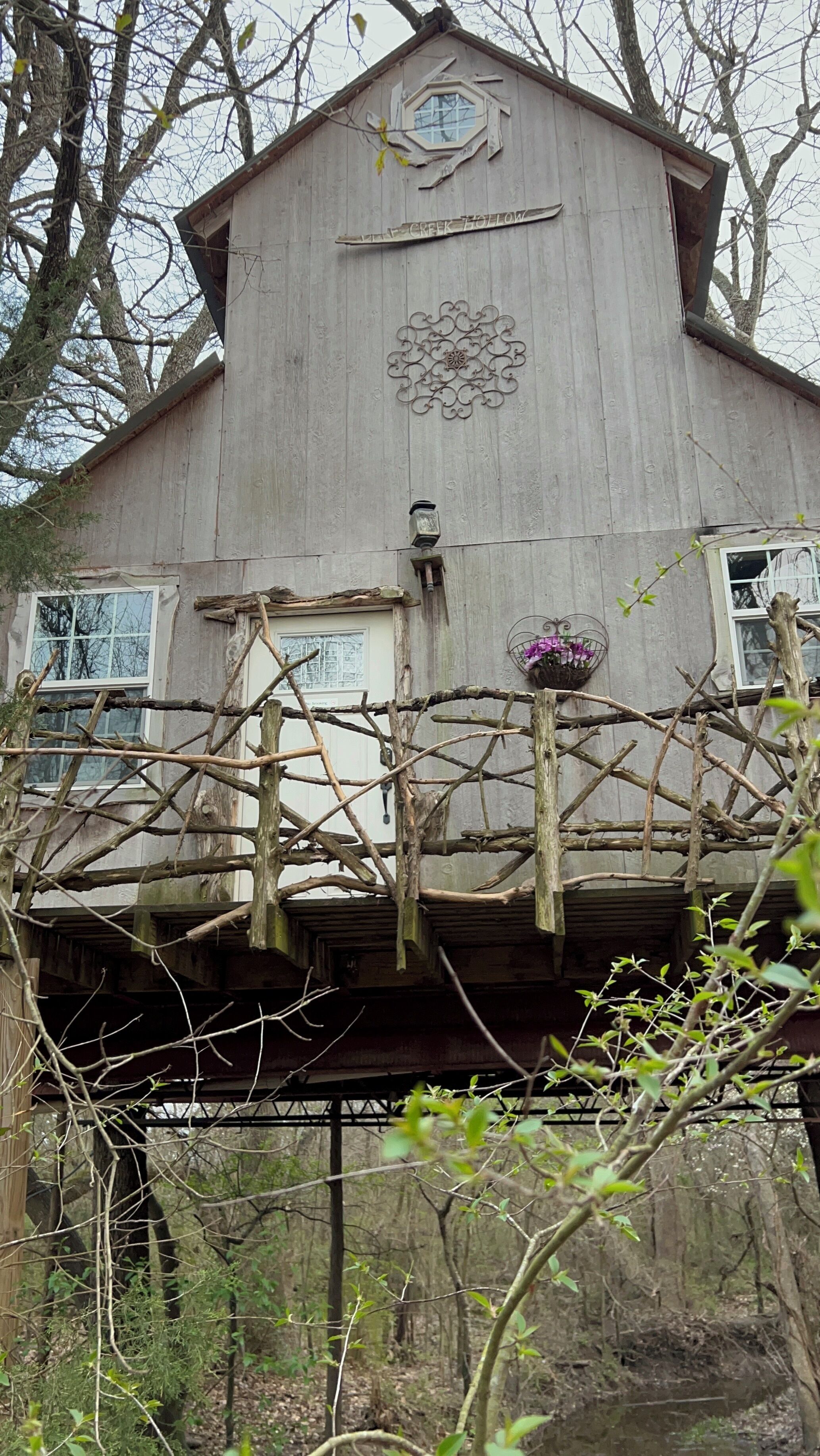 A wooden cabin with a sign reading "CREEK HOLLOW" and a decorative metal piece above the entrance.